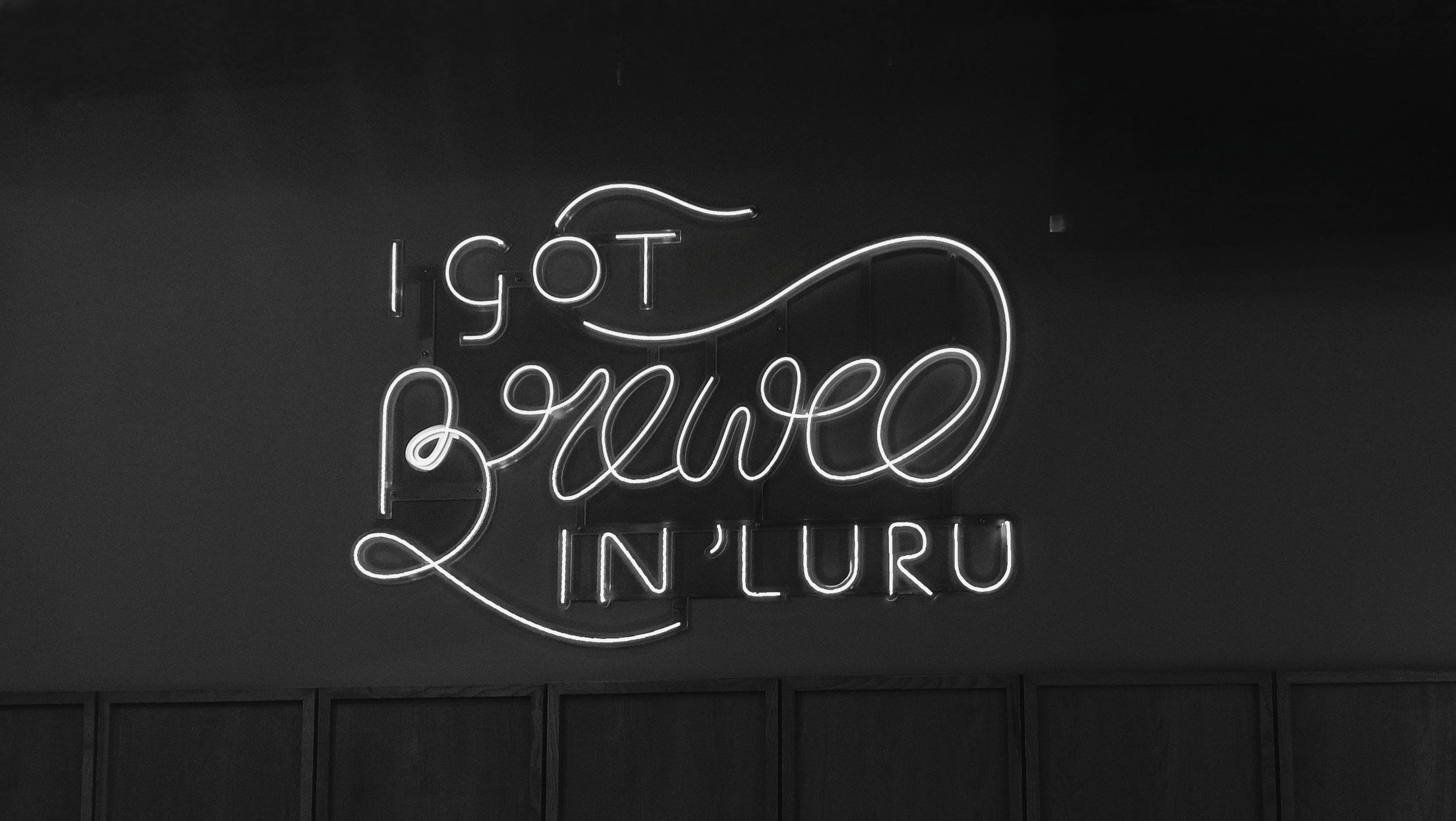 A glowing neon sign reading Brewed in Luru on a dark cafe wall