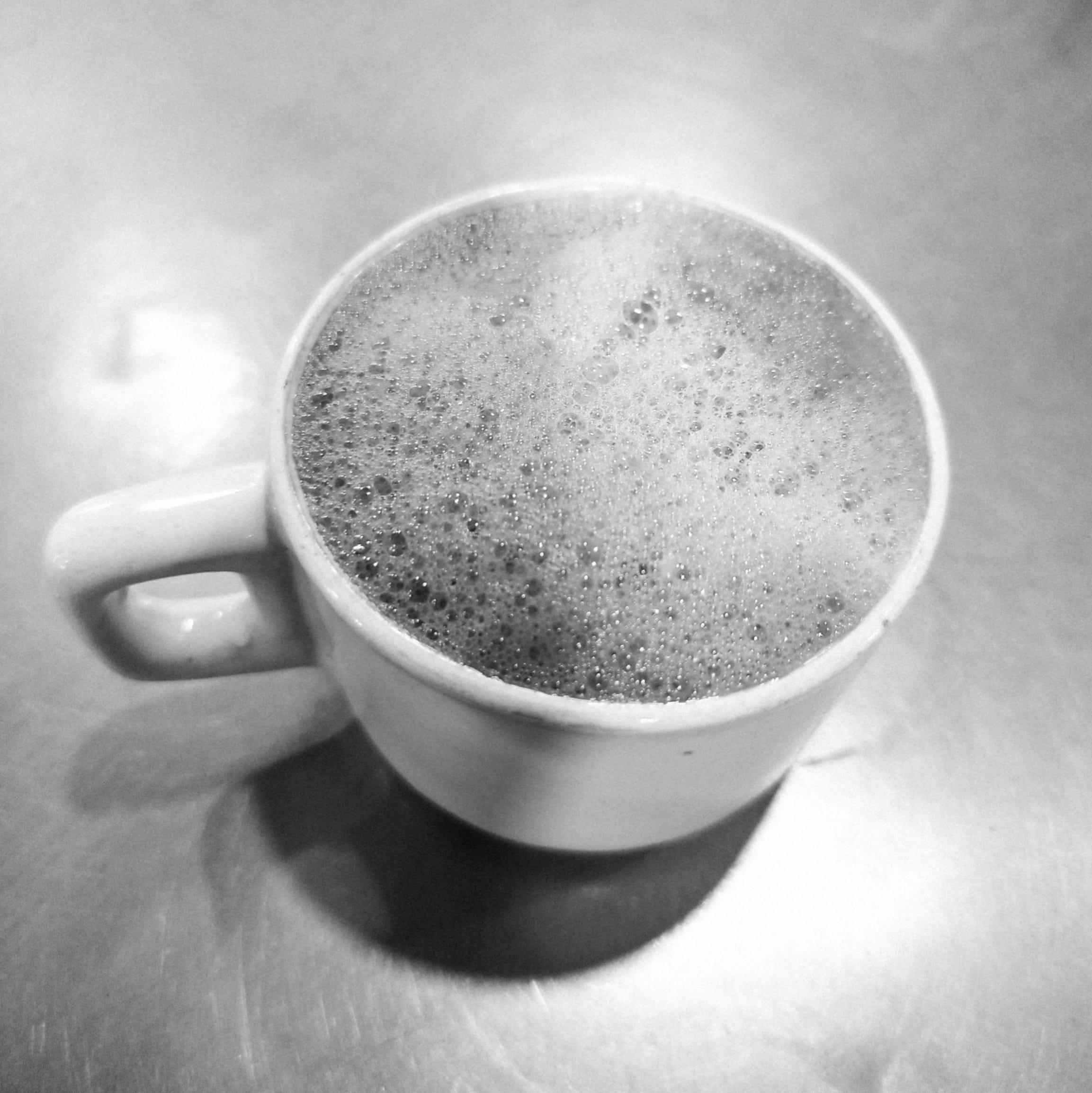A white cup of espresso with thick crema on a metal tabletop