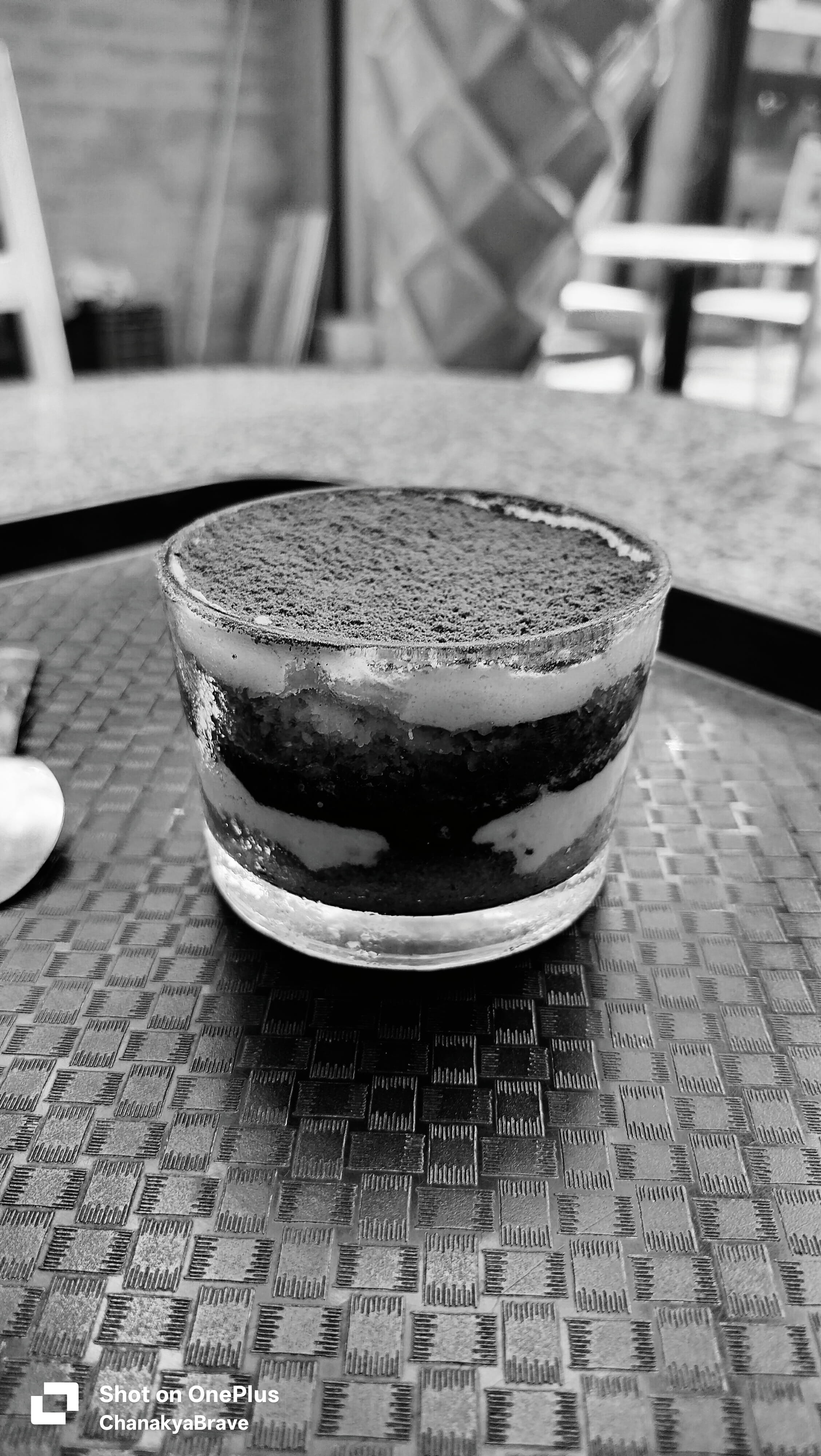 A layered tiramisu dessert served in a glass on a cafe tray